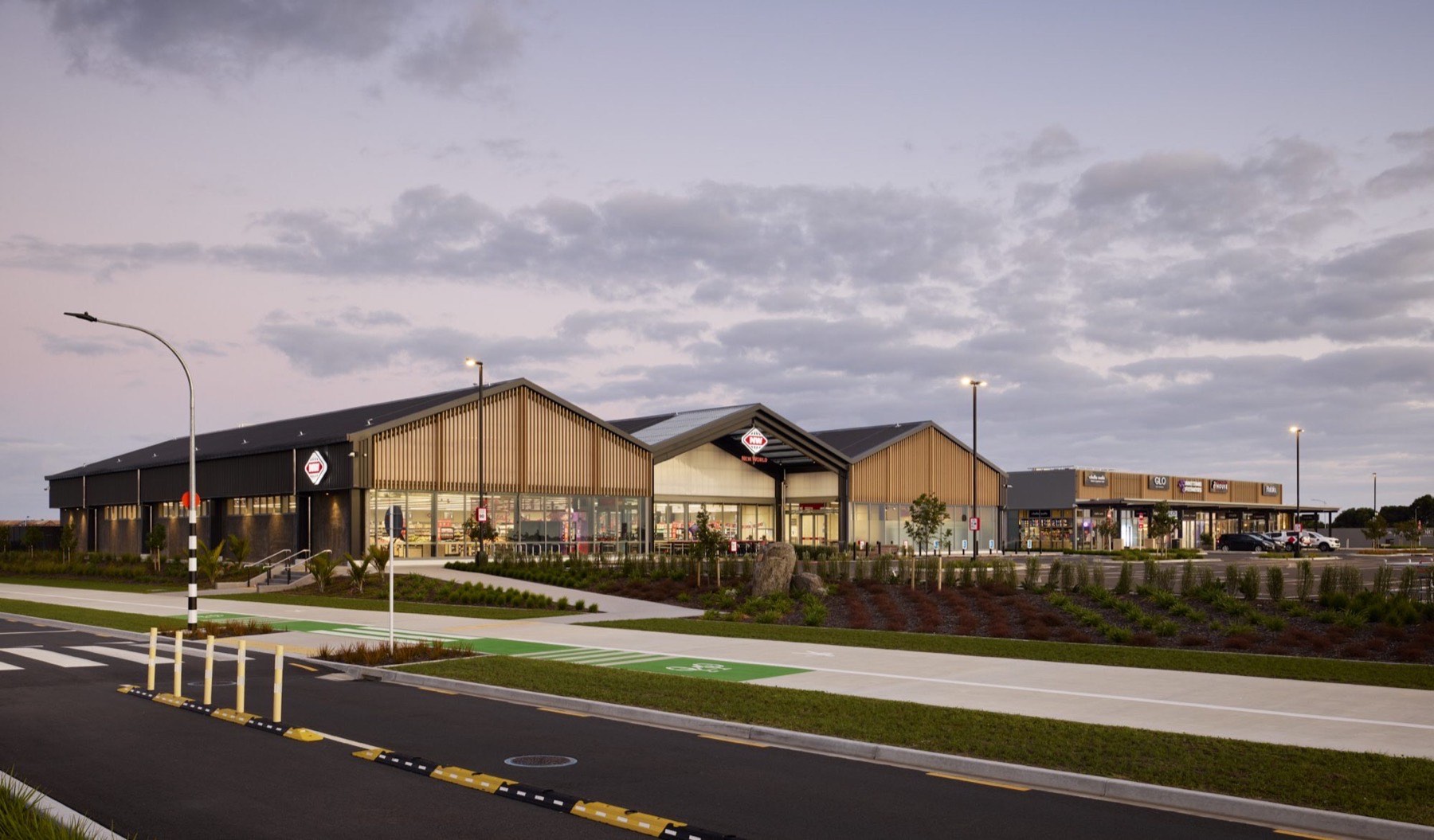 New World supermarket building at dusk with a dark long-run metal roof and timber-clad gables